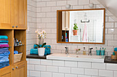 Waschbecken mit Ablage, darüber Wandspiegel und Holzschrank mit Regal im Badezimmer mit weißen U-Bahn-Fliesen im Dachgeschoss