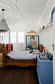 Antique wooden bed next to blue chest of drawers and large portrait of boy on wall