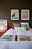 Scatter cushions and fabric samples on bed below pictures on dark wall in bedroom