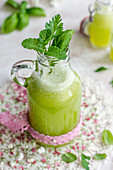 Green juice with basil and mint in a bottle with a pink ribbon