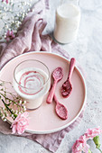 Ein Glas warme Milch daneben rosa Löffel aus Ruby-Schokolade