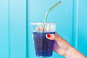 Woman holding blue drink in plastic cup with metal straw