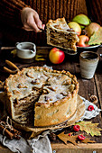 High autumn apple pie, in the background a person in a sweater holds a piece of cake