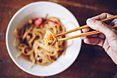 Person holding shrimp by wooden chopsticks while enjoying noodles