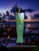 Green cocktail with ice cubes against a sunset