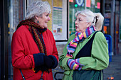 Two friends chatting whilst waiting at the bus stop