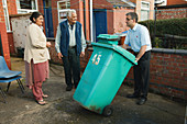 Son helping elderly south Asian parents by putting bin out