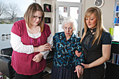 Carer and hairdresser helping old woman to sit down