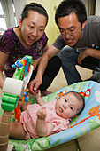 Chinese parents playing with baby in baby bouncer