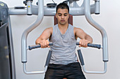 Young man using a chest press at gym