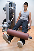 Young man using the leg extension equipment at gym