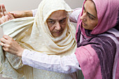 Young female carer helping an older woman put on her sari