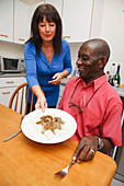 Elderly black man with carer serving his dinner