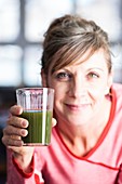 Smiling woman holding a glass of green smoothie
