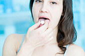 Young woman with pill on tongue