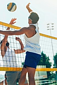 Male beach volleyball players jumping to hit the ball