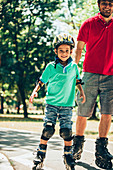 Father roller skating in park with son