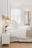 Golden pendant lamps flanking bed in white bedroom
