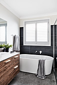 Frei stehende Badewanne unter Fenster und Waschtischunterschrank mit Holzfront im Bad