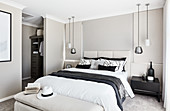 Double bed with tall headboard, pendant lamps above bedside tables and view into dressing area in elegant bedroom