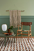 Macrame wall hanging above chair and low round table on patterned carpet