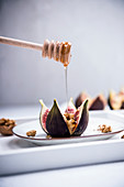 An oven-baked fig filled with walnuts and almond cheese being drizzled with syrup (vegan)