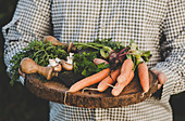 A man holding a wooden plater of freshly harvested vegetables