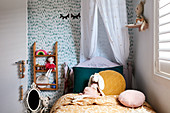 Bed with canopy and patterned wallpaper in girl's bedroom