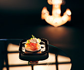 A salmon canapé on a serving platter on a dark surface
