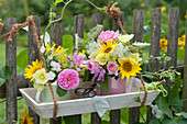 Kleine Sträuße aus Rosen, Sonnenblumen, Malven, Stockrosen, Wicken, Fenchelblüten und wilder Möhre am Gartenzaun