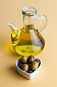 Jug of olive oil with olives in heart shaped dish
