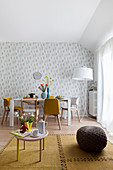 View past coffee table and pouffe into dining area with floral wallpaper