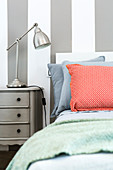 Red-patterned scatter cushion on bed against grey-and-white striped wall
