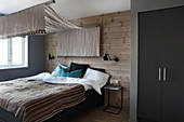 Bedroom in earthy shades with canopy over bed and wood-clad walls