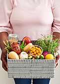 A woman holding a basket with vegetables, food and herbs