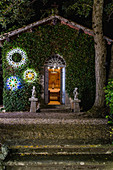 Cherubs flanking doorway of chapel with illuminated wreaths on wall