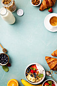 Breakfast with granola, yogurt, honey, fresh bananas, berries, chia seeds in bowl, coffee and croissants