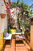 Small balcony with yellow wall tiles, boxy iron furniture and climber-covered pergola