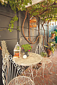 Romantic, metal garden furniture against wall below pergola