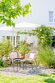 Two wicker chairs and side table on gravel terrace in late-summer garden