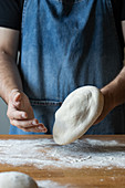 Unrecognizable male in apron flattening soft dough over table with flour while cooking pizza