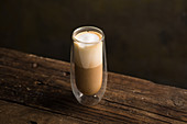 From above delicious fragrant brown beverage with white foam in glass cup on wooden table
