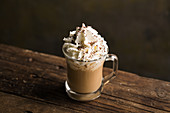From above delicious fragrant brown beverage with white cream and chocolate sprinkles on top in glass cup on wooden table
