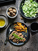 Skirt Steak mit schwarzem Knoblauch und Süßkartoffelsticks dazu Gurken-Eisbergsalat