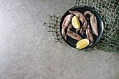 Raw uncooked squids calamari on ceramic plate with lemon and fishing nets
