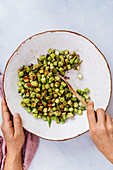 Stirring okra slices with spice mixture in a ceramic bowl