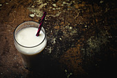 Tall glass of white milk with bright striped straw on table over black background