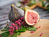 Ripe whole half and sliced figs among flavored green leaves of herbs and colorful flowers