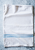 A white tea towel with blue stripes on a stone surface