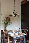 Rustic dining table and various chairs below wrought-iron chandelier
